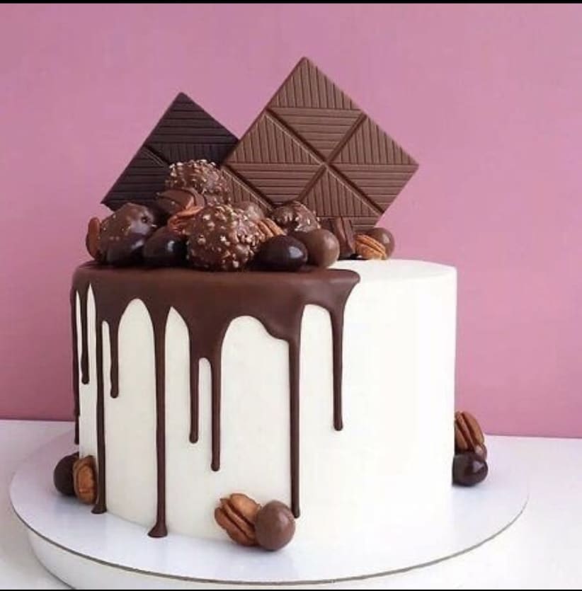 Designer white, round cake with chocolate drizzles, chocolate berries and chocolate bars